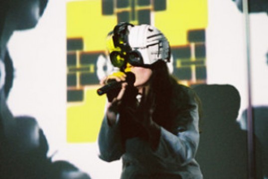 A woman wearing a helmet grips a microphone, poised to participate in an event