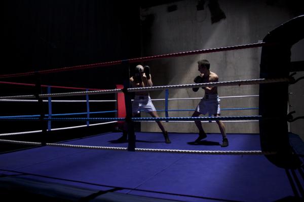Two boxers face off in a dimly lit boxing ring